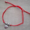 PULSERA DE HILO ROJO AJUSTABLE CON BOLITAS Y DIJE CORAZÓN DE ACERO.