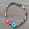 PULSERA DE TANZA CON MOSTACILLAS MULTICOLOR Y OJO TURCO CELESTE CON TERMINAL DE ACERO. LARGO 18 + 3 CM EXT.