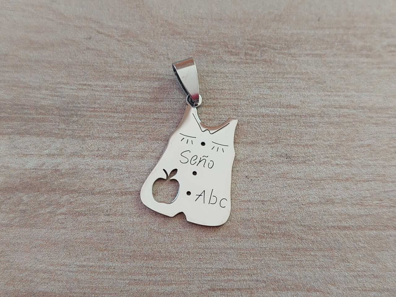 DIJE DE ACERO GUARDAPOLVO SEÑO CON MANZANA CALADA. MEDIDAS 19 X 25 MM