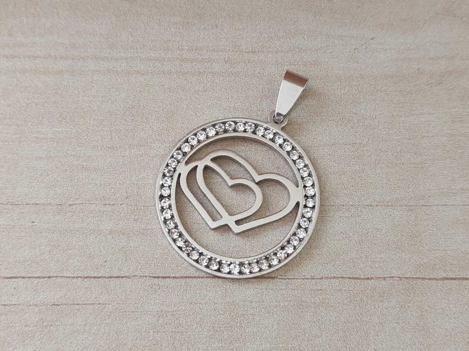 DIJE DE ACERO CIRCULO CON STRASS Y DOBLE CORAZÓN CALADO. TAMAÑO 30 MM .