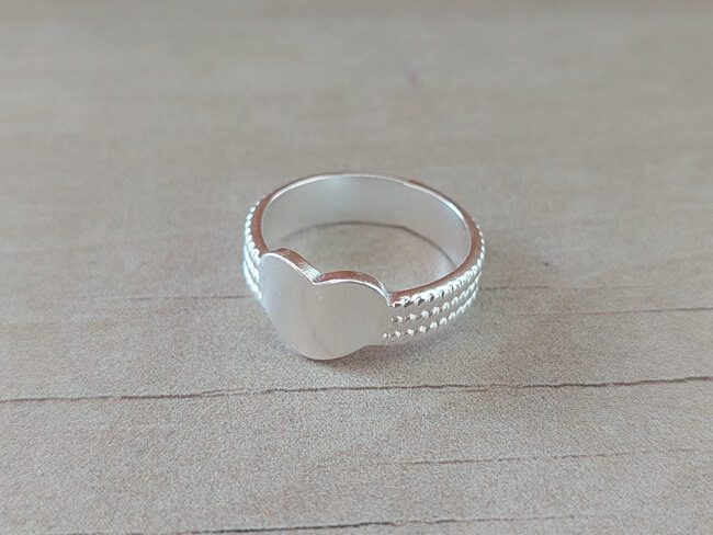 ANILLO DE ACERO BLANCO CINTA LABRADO CON CORAZÓN CENTRAL.
