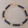 PULSERA DE TANZA CON MOSTACILLAS NEGRAS, DOS BOLITAS 3 MM INTERCALADAS Y TERMINAL DE ACERO DORADO. LARGO 18,5 CM.