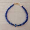 PULSERA DE TANZA CON MOSTACILLAS AZULES, OJO TURCO CENTRAL Y TERMINAL DE ACERO DORADO. LARGO 18,5 CM.