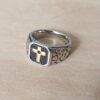 ANILLO DE ACERO ESTILO SELLO CON CRUZ DORADA Y DETALLES EN NEGRO.